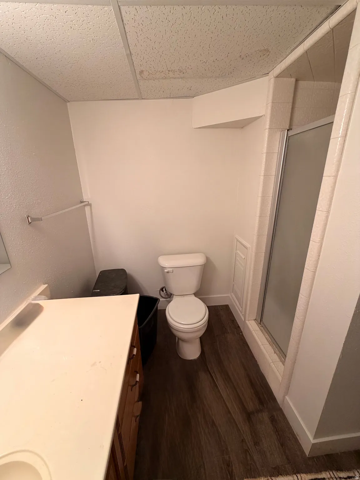 Bathroom featuring wood-finish flooring, a white toilet, and a glass-enclosed shower with tiled surround