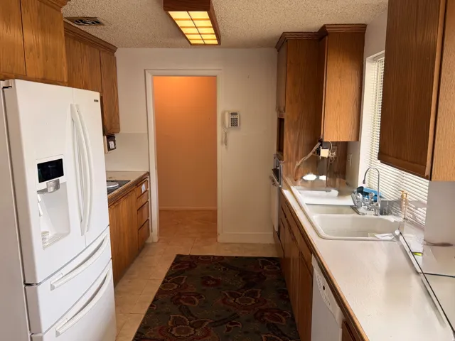 Galley kitchen featuring wood cabinetry, white countertops, a double basin sink, and tile flooring