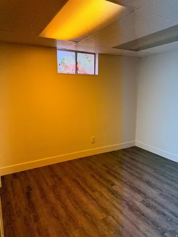 Room featuring wood-finish flooring, drop ceiling with recessed lighting, and a single window
