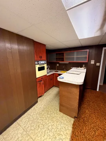 Compact kitchen area featuring wood paneling, wood cabinetry, a built-in oven, and a corner sink