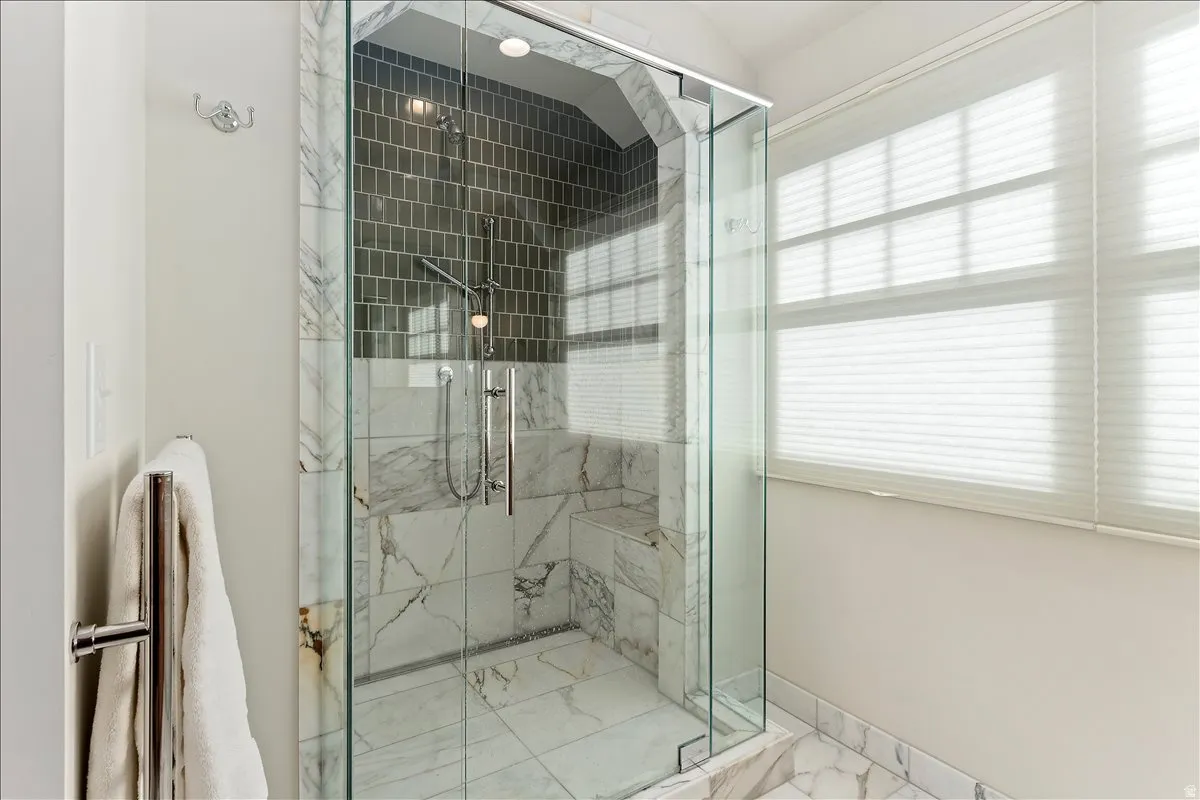 Glass-enclosed shower featuring marble-patterned tile walls, a built-in bench, and a rectangular tile accent band