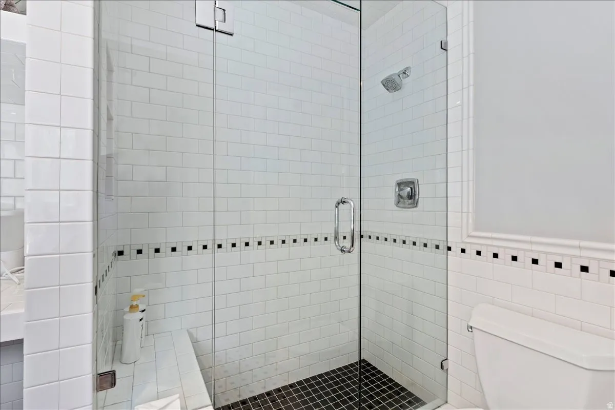 Enclosed shower with clear glass paneling featuring white subway tile walls and black mosaic tile flooring