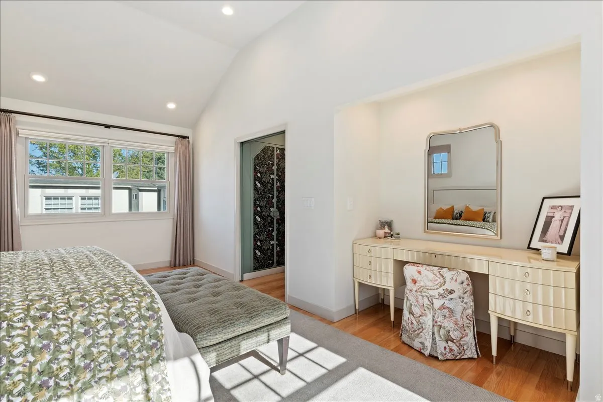 Vaulted ceiling bedroom featuring wood-finish flooring, recessed lighting, and a double window with exterior building views