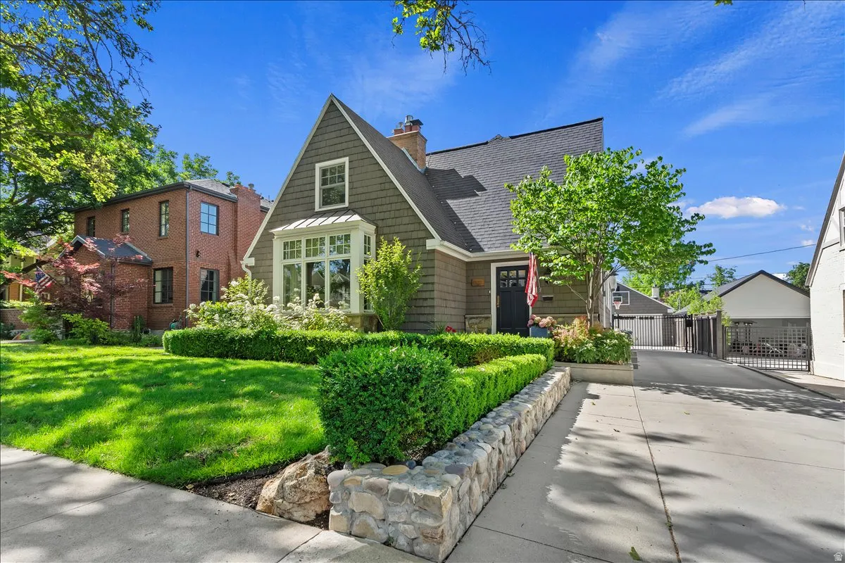 Craftsman-style home featuring a shingle siding exterior, an arched entry doorway, a prominent bay window, a manicured lawn, and a stone-clad retaining wall
