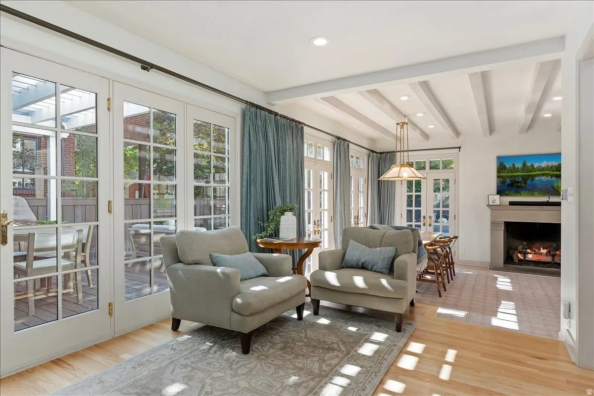 Living area featuring multiple sets of white French doors, wood-finish flooring, a beamed ceiling, recessed lighting, and a stone fireplace with a mantle