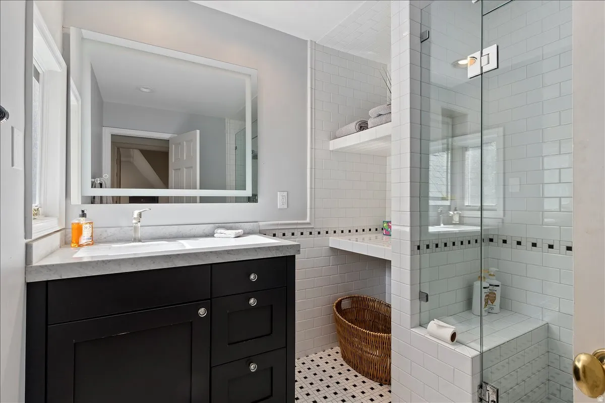 Bathroom featuring a black vanity with a white countertop and an undermount sink, a framed mirror, and a glass-enclosed shower with white subway tile and a built-in bench