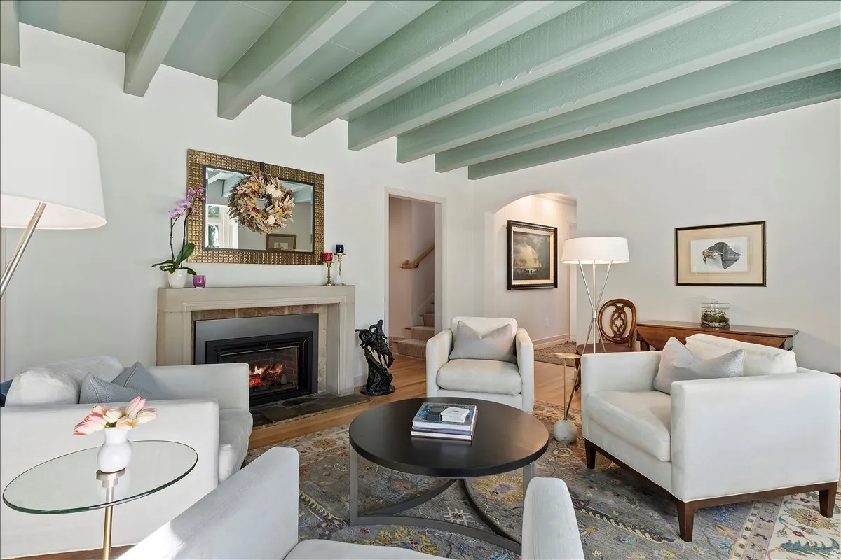 Living area featuring a stone fireplace with a black insert, light wood-finish flooring, and a coffered ceiling with painted beams