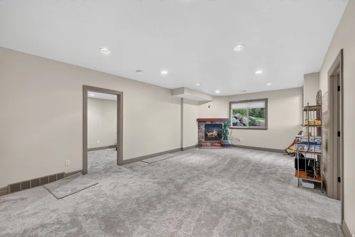Spacious carpeted room featuring a stone-faced fireplace with a wood mantel, recessed lighting, and a window providing natural light