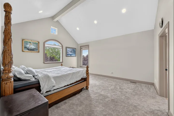 Spacious room featuring vaulted ceilings with exposed beam, recessed lighting, arched window, and plush carpet flooring