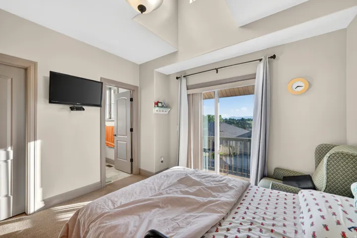 Bedroom featuring a sliding glass door to a private balcony, vaulted ceiling, neutral paint finishes, and soft carpet flooring