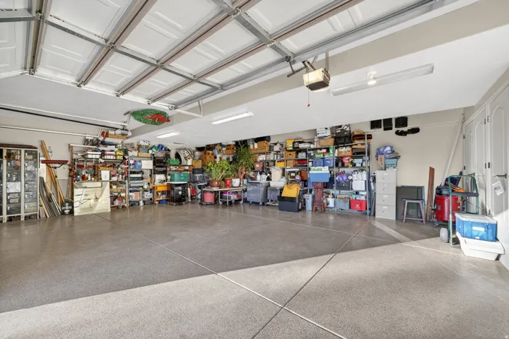 Spacious garage with an epoxy-coated concrete floor, white paneled garage doors, and multiple fluorescent light fixtures