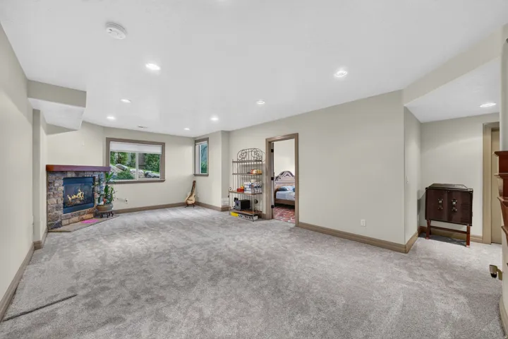 Spacious room featuring plush gray carpeting, a stone-surround fireplace with a wood mantle, and recessed lighting