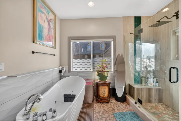 Modern bathroom featuring a freestanding soaking tub with chrome fixtures, a glass-enclosed shower with a rain showerhead, a built-in shower bench, and mixed tile flooring