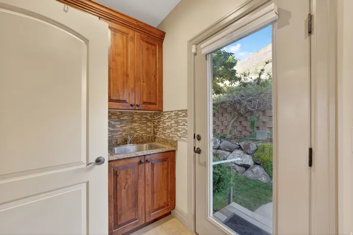 Utility sink area featuring wood-finish cabinetry, a granite-finish countertop, and a mosaic tile backsplash