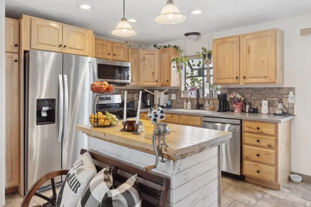Kitchen featuring wood-finish cabinetry, stainless steel appliances, a tile backsplash, and a central island with a butcher block countertop