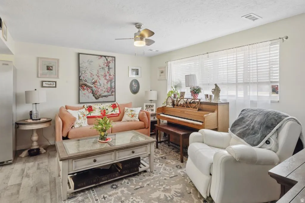 Spacious living area featuring light-toned walls, wood-finish flooring, and a ceiling fan with integrated lighting