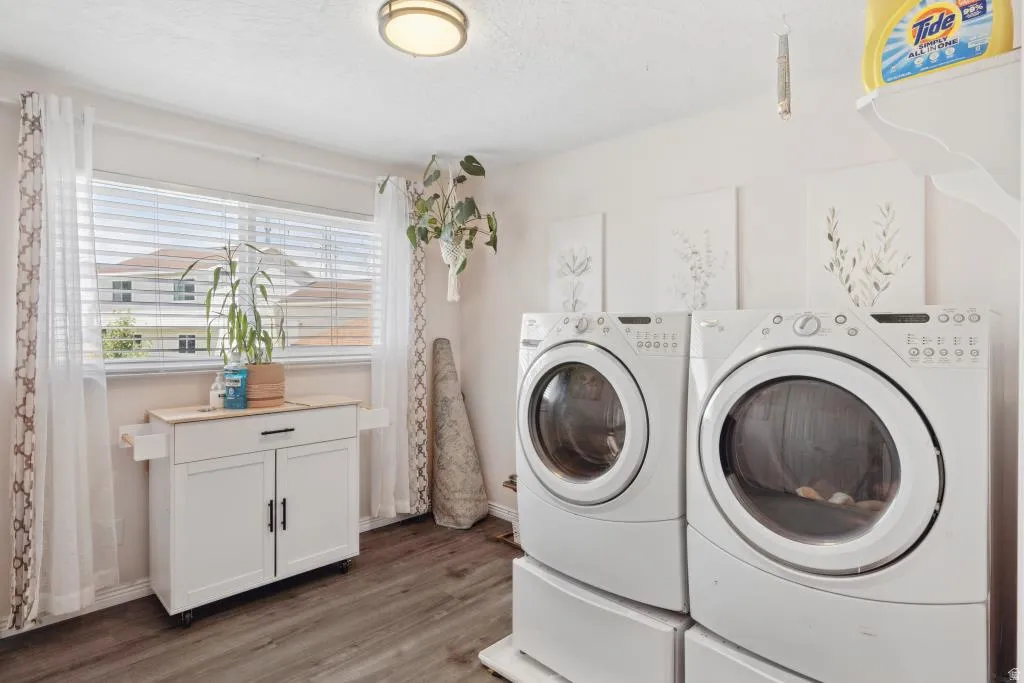 Bedroom turned laundry room. Dedicated laundry room featuring large window with blinds, wood-finish flooring, built-in shelving, and a modern ceiling light fixture