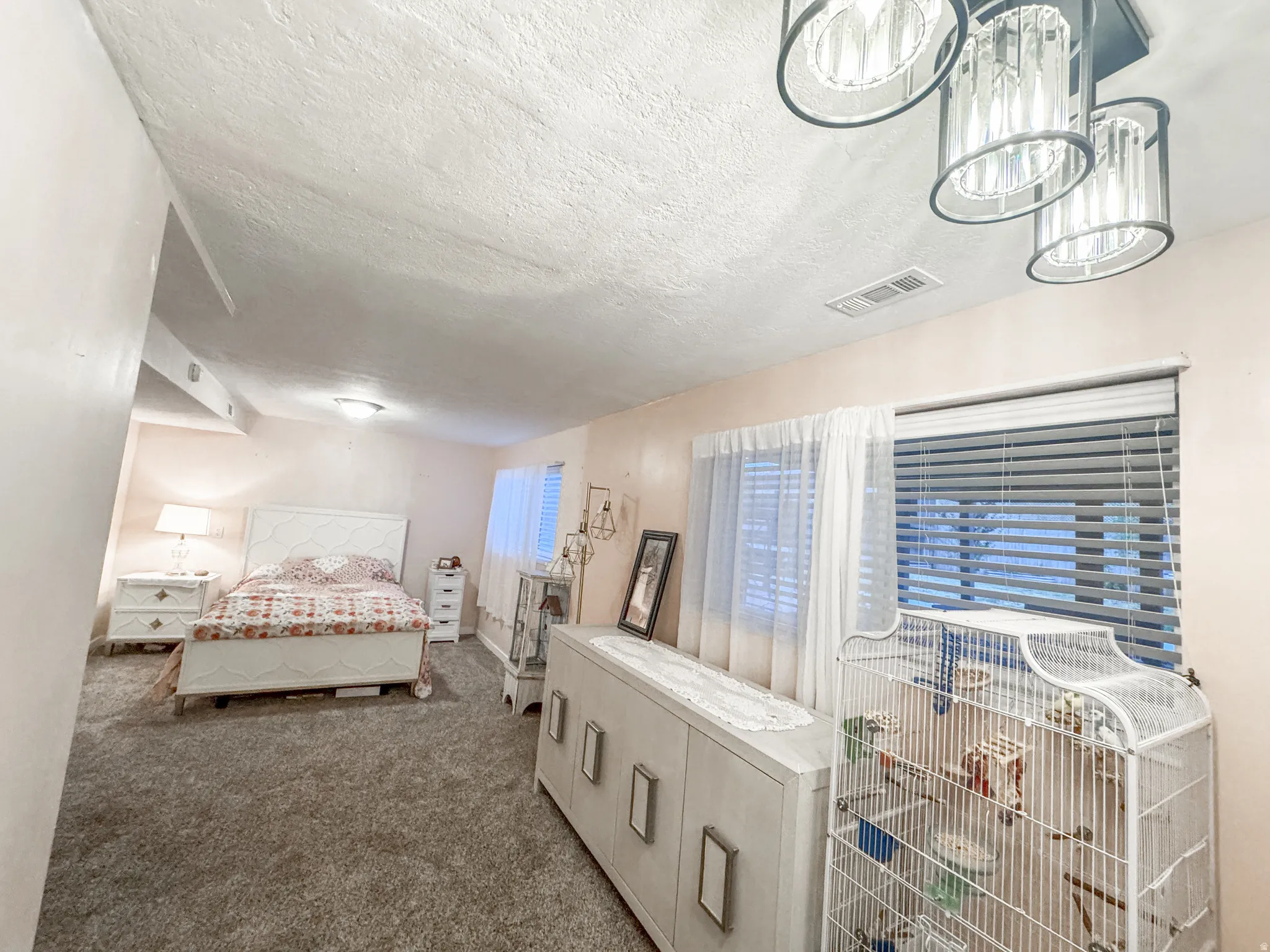 Bedroom featuring plush carpeting, a large window with blinds and sheer curtains, and a modern ceiling light fixture