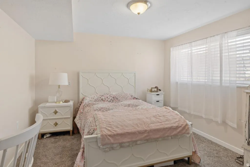 Bedroom featuring soft neutral wall paint and a window with blinds and sheer curtains