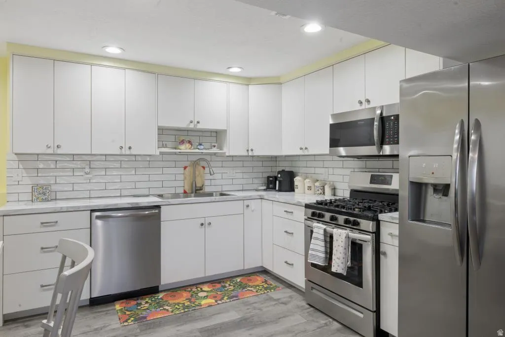 Modern kitchen featuring white cabinetry, subway tile backsplash, stainless steel appliances, and a double basin sink