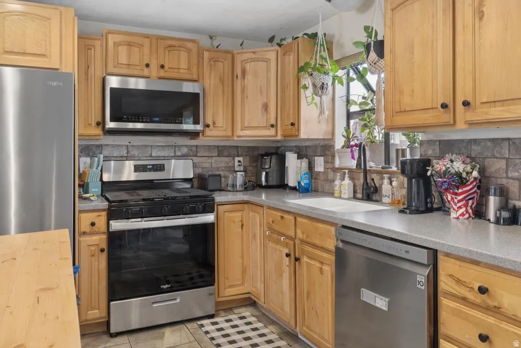 Kitchen featuring wood-finish cabinetry, stainless steel appliances, a tile backsplash, and a window above the sink