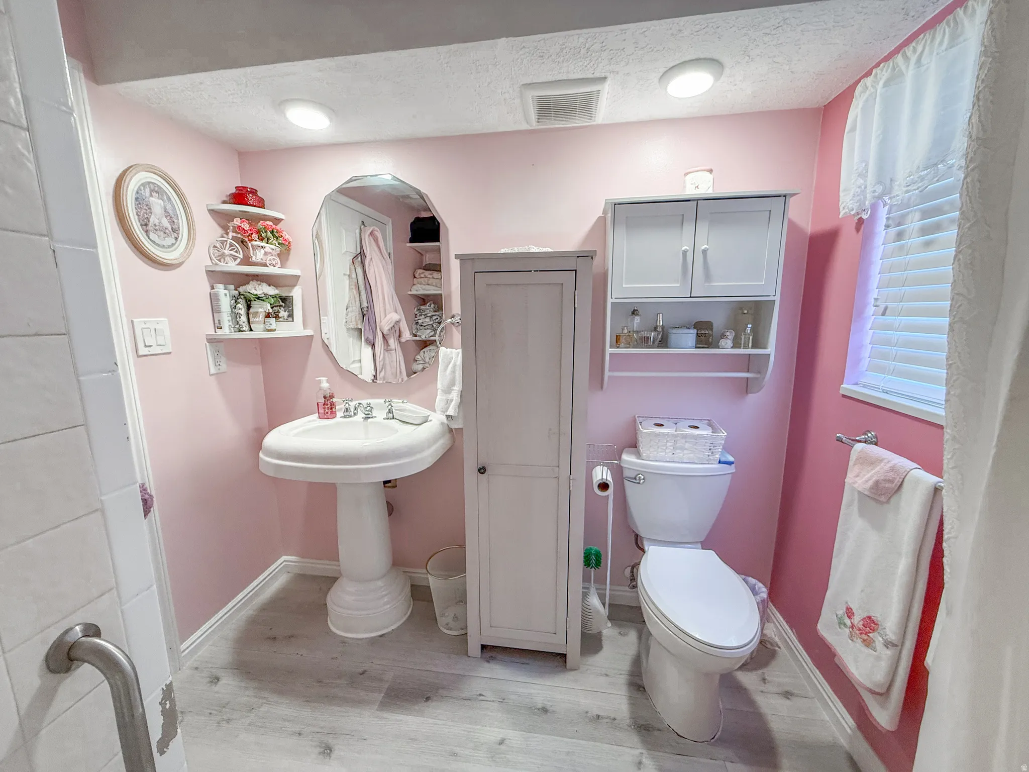 Bathroom featuring a pedestal sink, toilet, window with blinds, and wood-finish flooring