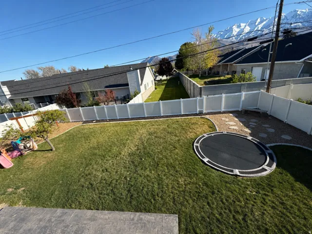 Expansive backyard with a manicured lawn, white vinyl fencing, and a stone-paver patio area