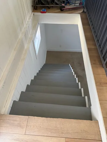 Stairwell with wood-finish flooring extending into the landing, featuring painted gray treads, white risers, and a window providing natural light