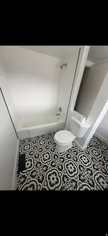 Bathroom featuring patterned floor tiles, white bathtub with a shower fixture, and a white toilet