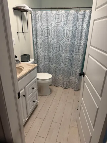 Bathroom featuring a white vanity with panel cabinetry and black hardware, a built-in toilet, and light-colored plank flooring