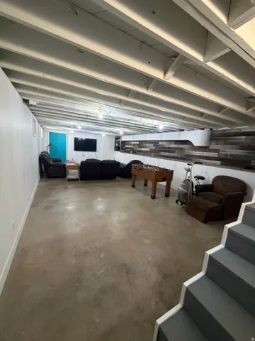 Spacious lower level featuring exposed ceiling joists, concrete flooring, and a decorative wood-panel accent wall
