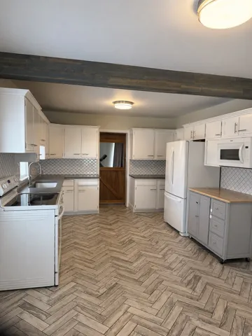 Kitchen featuring herringbone-pattern wood-finish flooring, white cabinetry, geometric tile backsplash, and a wood-finish ceiling beam