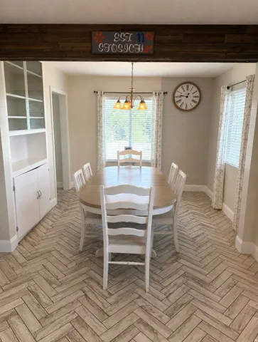 Dining area featuring herringbone-patterned tile flooring, a dark wood-finish ceiling beam, and a built-in cabinet with glass-fronted upper shelving