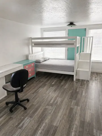 Bedroom featuring wood-finish flooring, white walls, and multiple windows with horizontal blinds