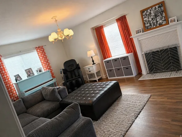 Living area featuring wood-finish flooring, a white fireplace with a patterned tile surround, and a classic chandelier