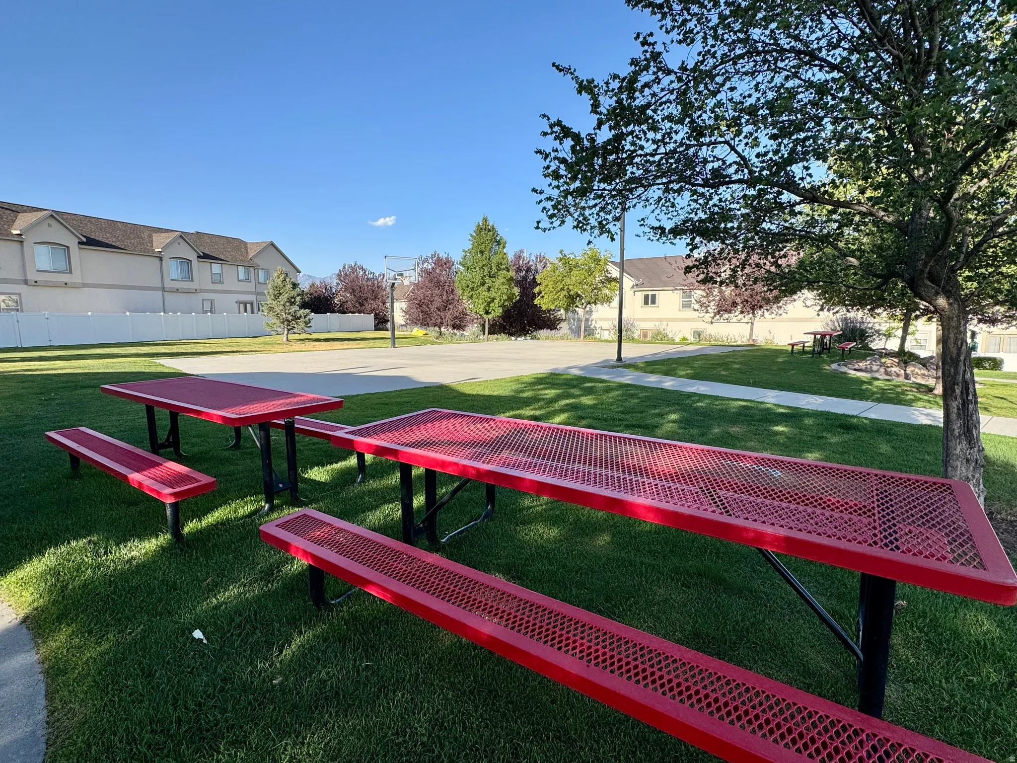 Community green space featuring multiple picnic tables, a paved basketball court, and mature trees providing shade