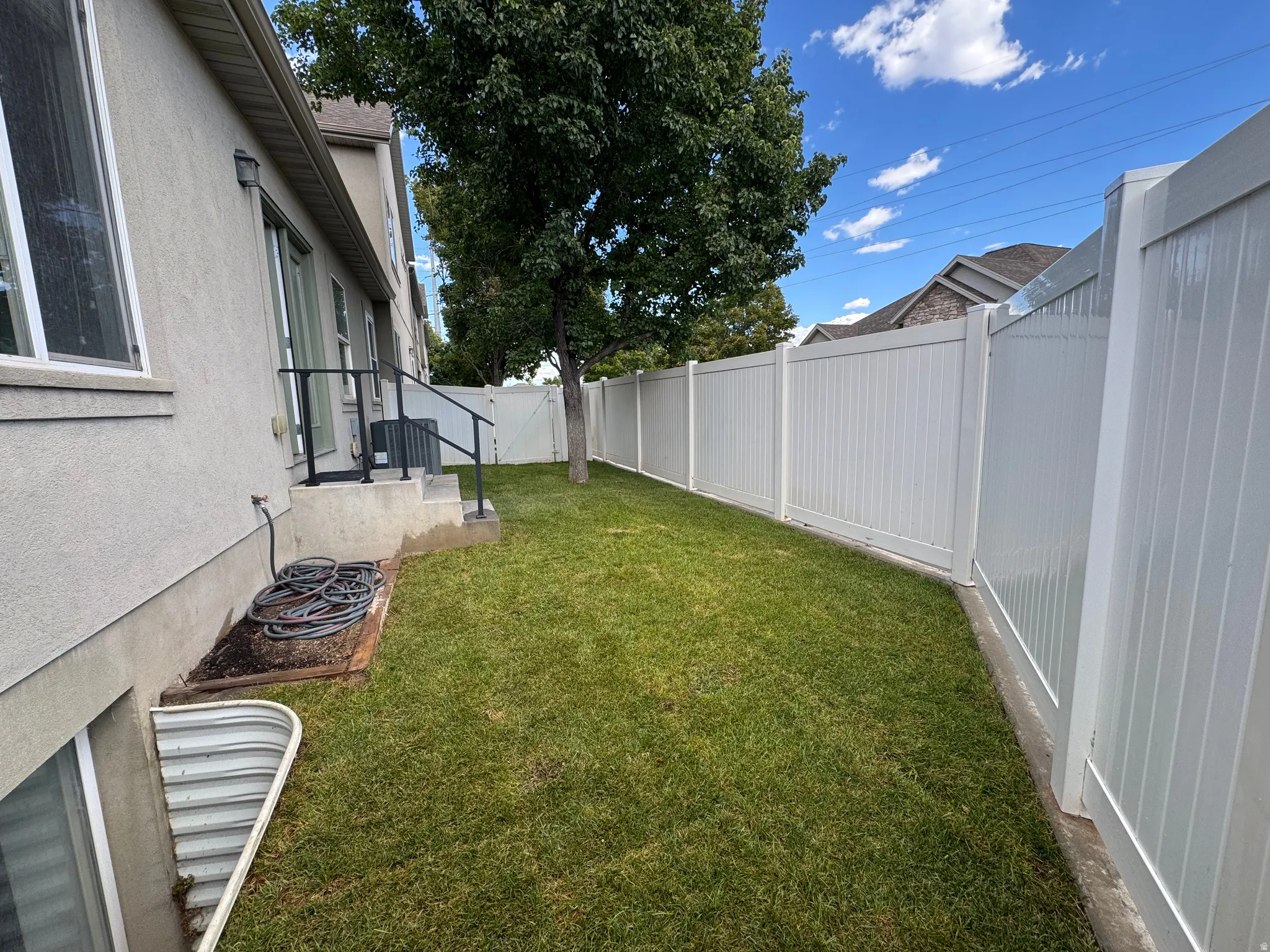 Manicured lawn, full privacy fencing, exterior stucco finish, and basement window well