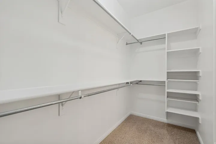 Primary bedroom walk-in closet featuring white built-in shelving, multiple hanging rods