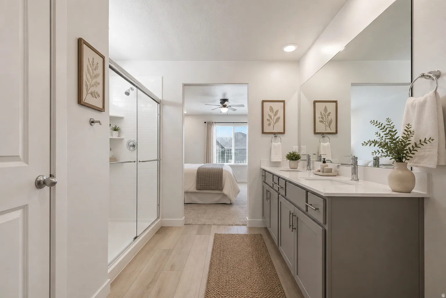Bathroom featuring a dual vanity with grey cabinetry and light countertops, a large frameless mirror, and a glass-enclosed shower
