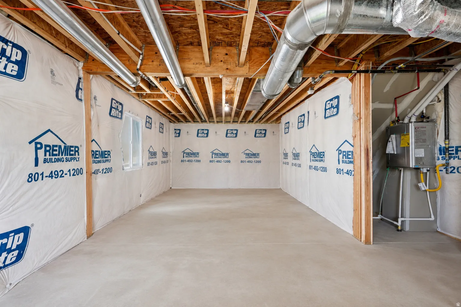 Unfinished basement with exposed ceiling joists and ductwork, featuring a poured concrete floor and a visible water heater installation