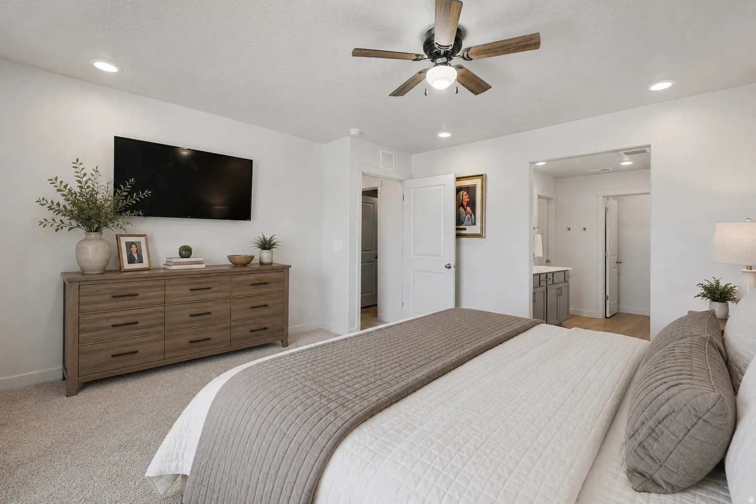 Carpeted bedroom featuring a ceiling fan with light fixture, recessed lighting, and an entryway to a bathroom with wood-finish flooring and a vanity with a sink