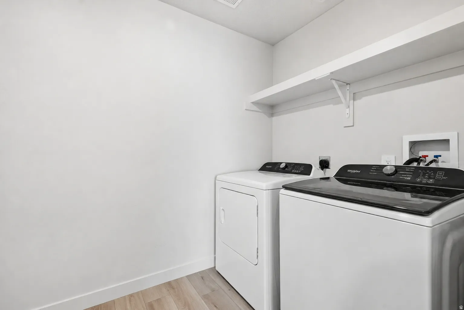 Dedicated laundry area featuring a white wall shelf, wood-finish flooring, and light-toned walls