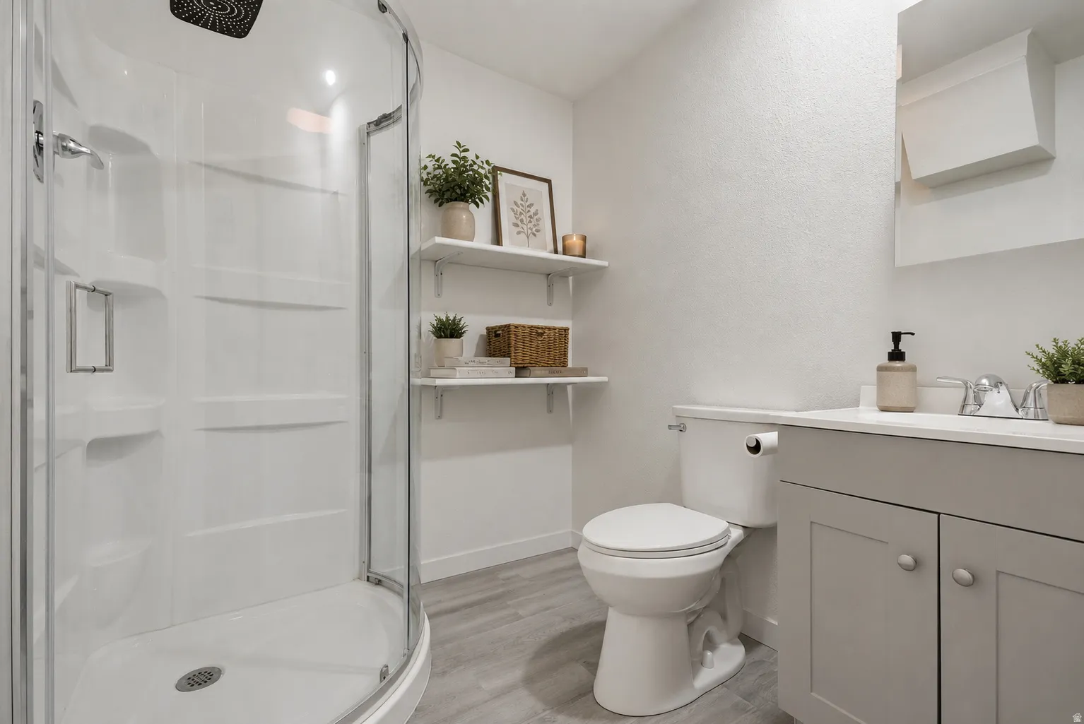 Three-piece bathroom featuring a curved glass shower enclosure, a single vanity with a light gray cabinet, a white countertop, and wood-finish flooring