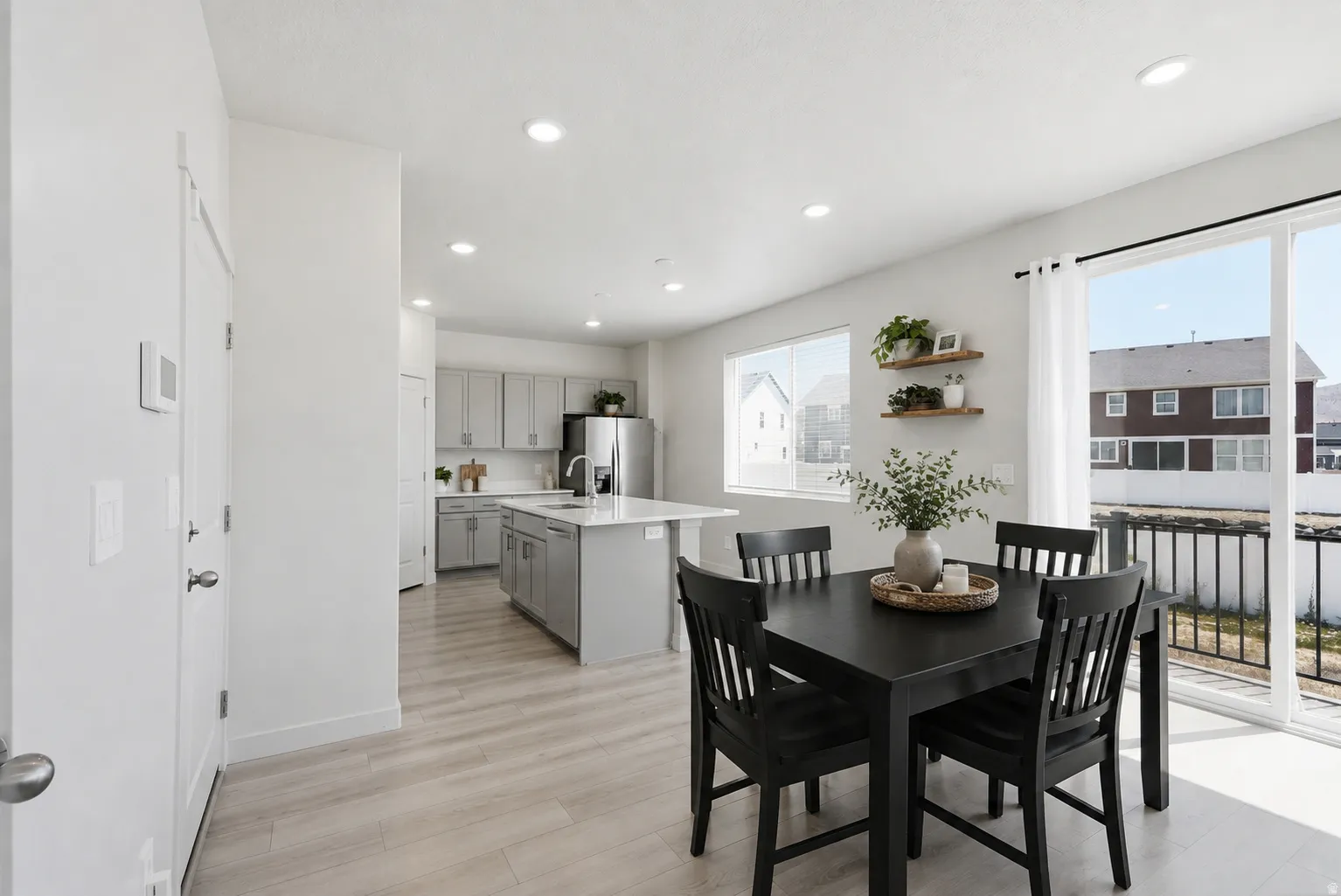 Open-concept living area featuring light wood-finish flooring, recessed lighting, a modern kitchen with light gray cabinetry and stainless steel appliances, and a dining space with direct access to an outdoor area via a sliding glass door