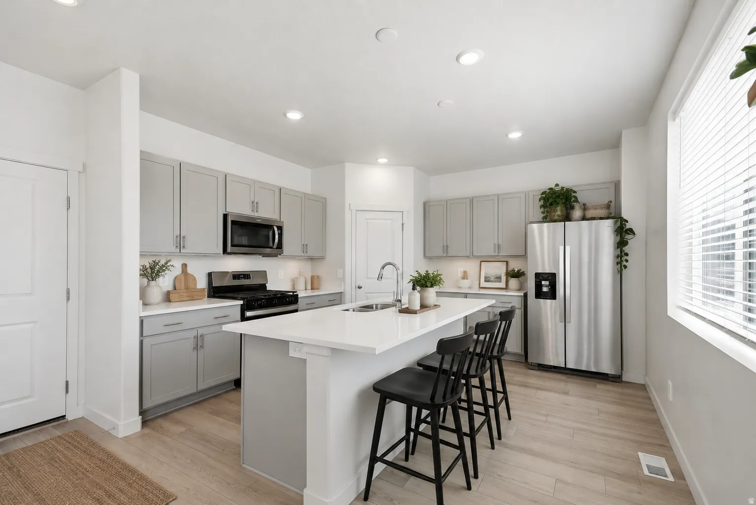 Modern kitchen featuring light gray cabinetry, stainless steel appliances, a center island with sink, and wood-finish flooring
