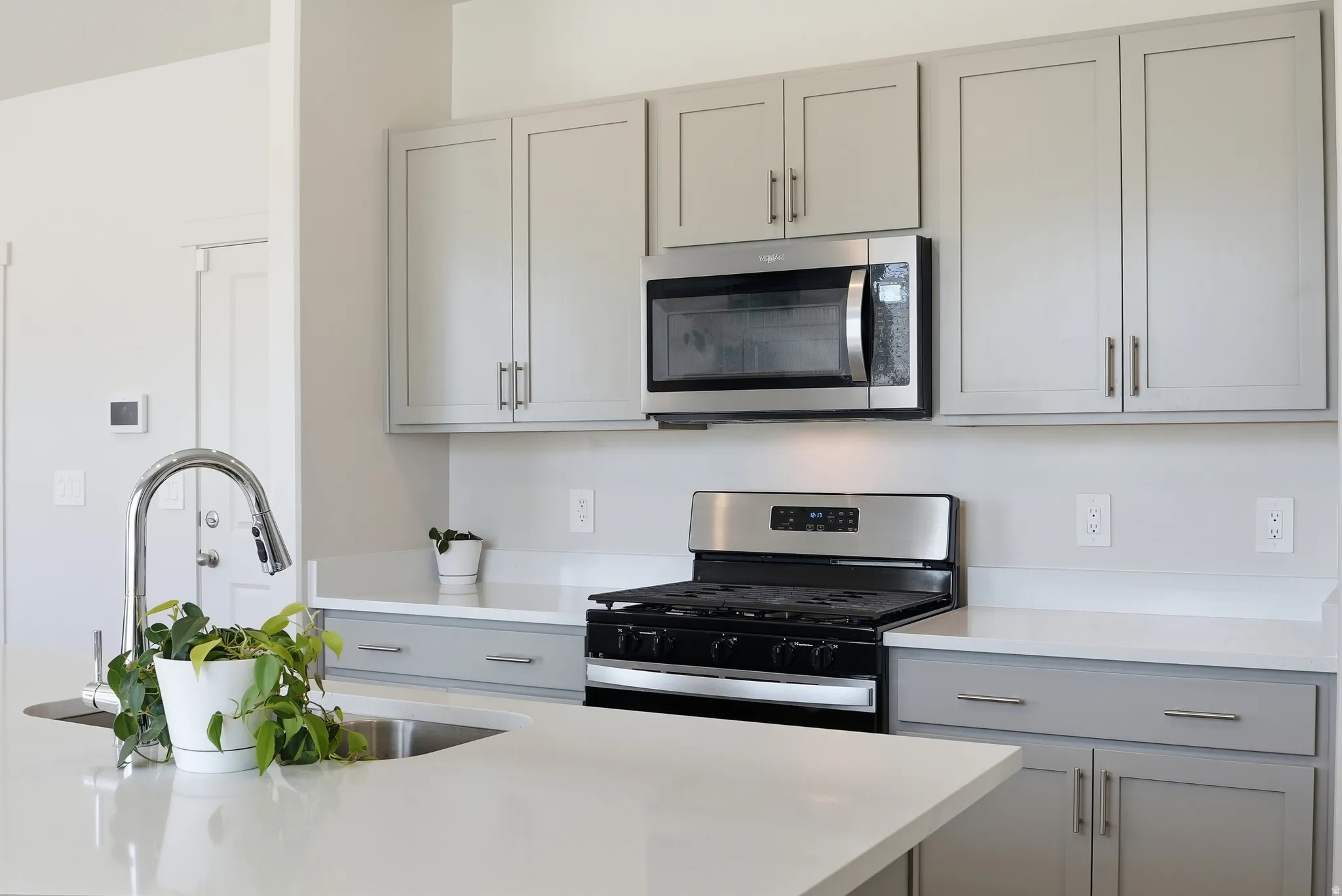 Kitchen featuring a stainless steel gas range, over-the-range microwave, light gray cabinetry with brushed nickel hardware, and light-toned countertops
