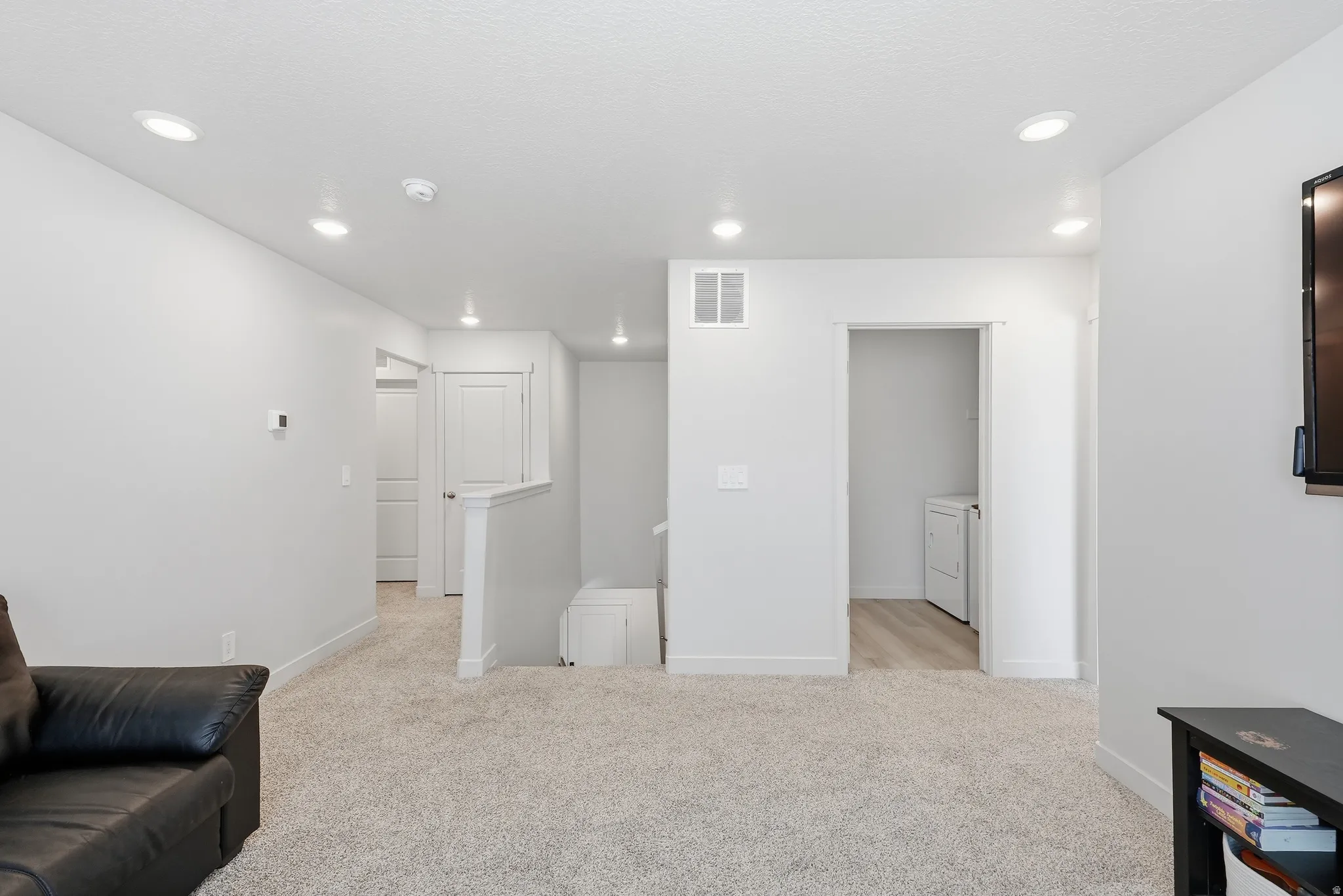 Carpeted area featuring recessed lighting, light gray wall paint, white trim, and a doorway revealing wood-finish flooring