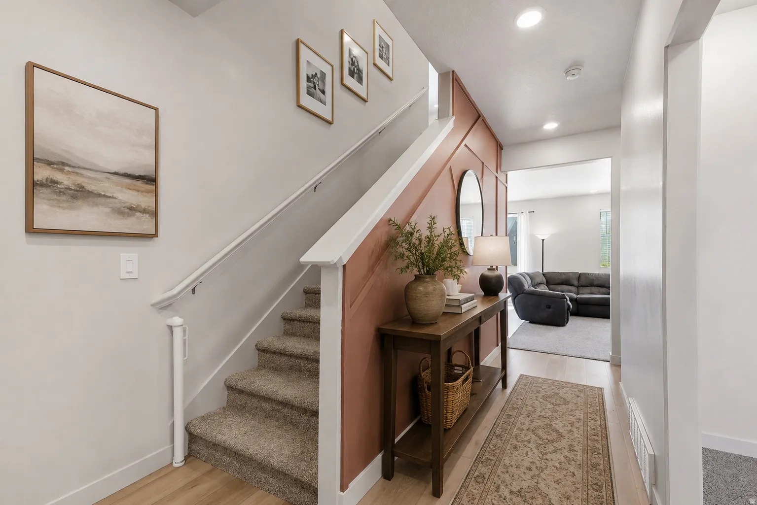 Entryway featuring wood-finish flooring, a carpeted staircase with white railing, and a feature wall with decorative paneling