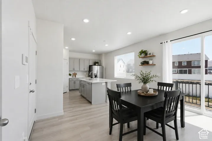 Open-concept living area featuring light wood-finish flooring, recessed lighting, a modern kitchen with light gray cabinetry and stainless steel appliances, and a dining space with direct access to an outdoor area via a sliding glass door