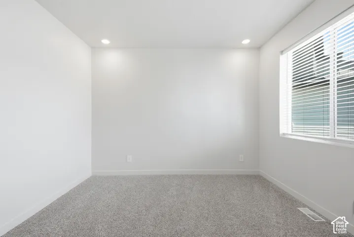 Bright room featuring light gray carpeting, white walls, recessed ceiling lighting, and a window with horizontal blinds